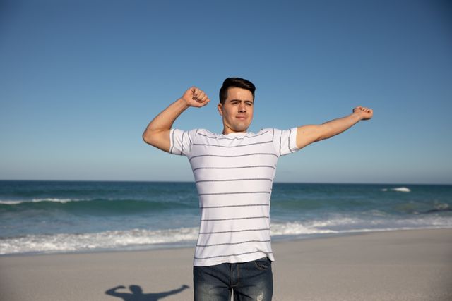 Caucasian man enjoying time at the beach on a sunny day with blue sky, stretching his arms. Summer Beach Vacation. 