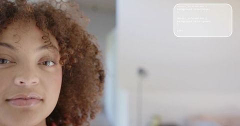 Curly-haired woman looking at camera with code overlay and home office copy space