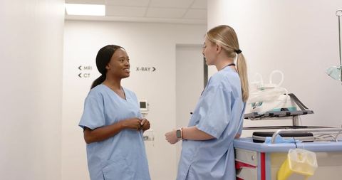 Black and white nurses talking in hospital corridor near mri ct x-ray signs