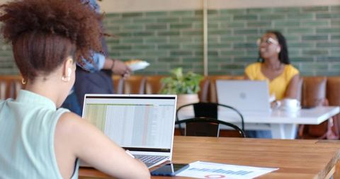 African american woman working on spreadsheet laptop at cafe table, coworking focus