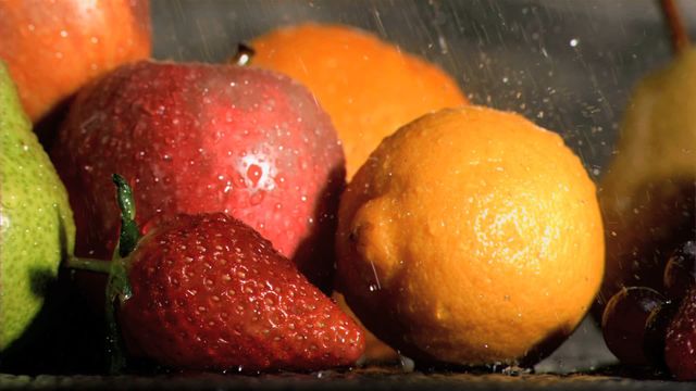 Fruits including strawberries, apples, and lemons are being showered with rain in slow motion. The water droplets create a fresh and appetizing look against the dark background. Ideal for use in advertisements for fresh produce, healthy eating campaigns, or products emphasizing natural ingredients.