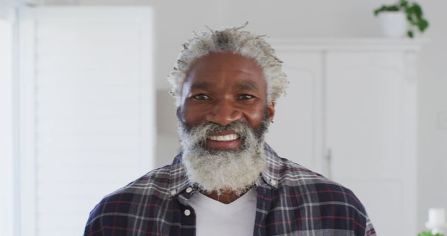 Portrait of happy African American senior man with white hair and beard at home, smiling to camera. Social distancing and self isolating at home during Coronavirus Covid 19 quarantine lockdown.