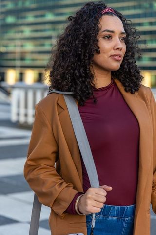 Confident urban woman standing on rooftop terrace wearing camel overcoat and maroon top