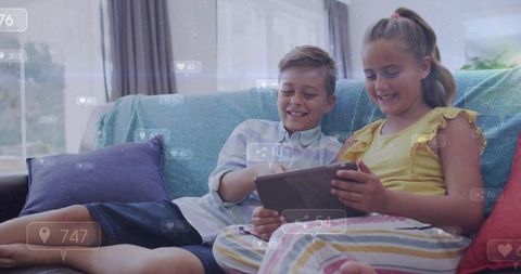 Siblings sharing tablet on couch smiling and playing together in bright home interior