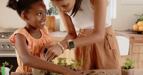 Mother and daughter planting seedlings together in kitchen
