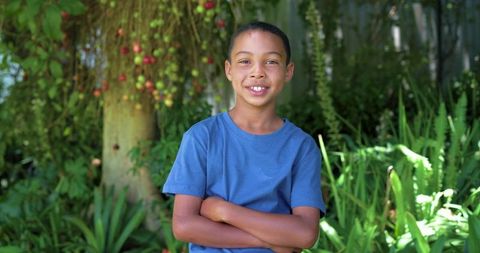 African american teen boy standing with arms crossed smiling in lush backyard garden