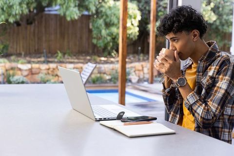 Young Man Relaxing with Coffee While Browsing Laptop Outdoors