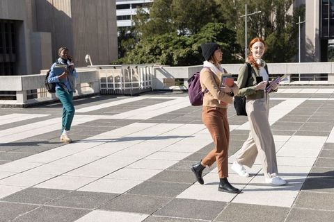 Diverse female students walking across sunlit campus plaza with backpacks and notebooks