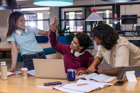 Multicultural students collaborating and high-fiving in modern campus study space