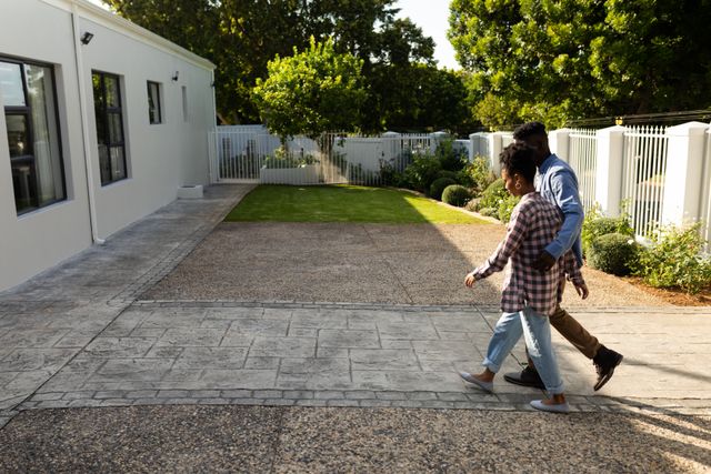 Side view of african american young woman with young boyfriend walking on footpath towards house. unaltered, lifestyle, love and togetherness concept.