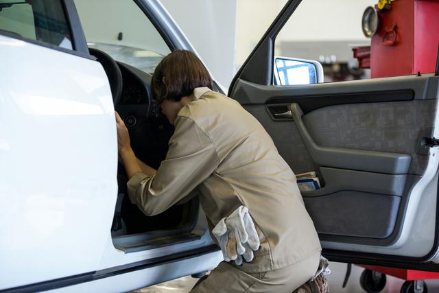 Female mechanic examining car interior at an auto repair shop. Ideal for use in articles about women in automotive industry, car maintenance tips, and professional automotive services. Suitable for illustrating concepts of vehicle inspection, repair services, and gender diversity in technical professions.