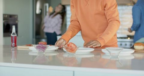 Friends preparing casual meal at modern kitchen island, man arranging plates with tomato