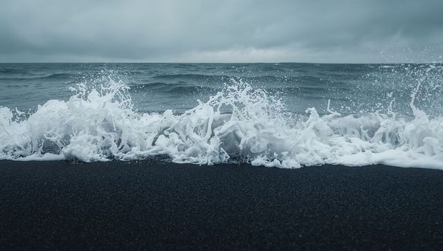 Foamy waves crashing onto black sand moody overcast coastline