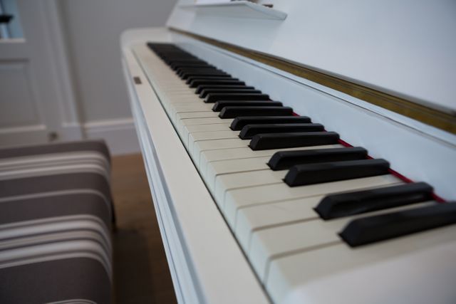 Close-up of white piano keys in a modern home setting. Ideal for use in articles or advertisements related to music education, home decor, musical instruments, or lifestyle blogs. The striped bench adds a touch of elegance and comfort, making it suitable for interior design inspiration.
