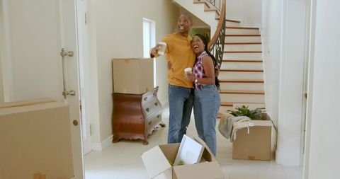 African american couple moving into new home holding coffee pointing toward staircase