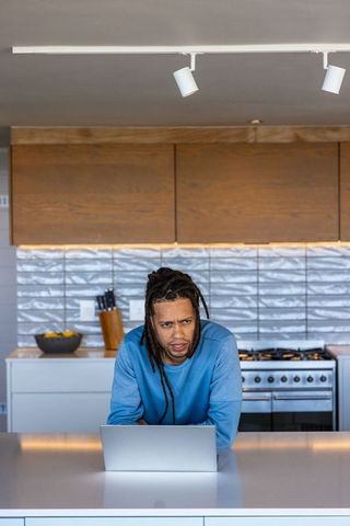 African american man leaning on kitchen island working on laptop in modern kitchen