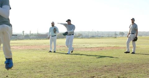 Sunlit amateur baseball team practicing on grass outfield wearing gray shirts and gloves
