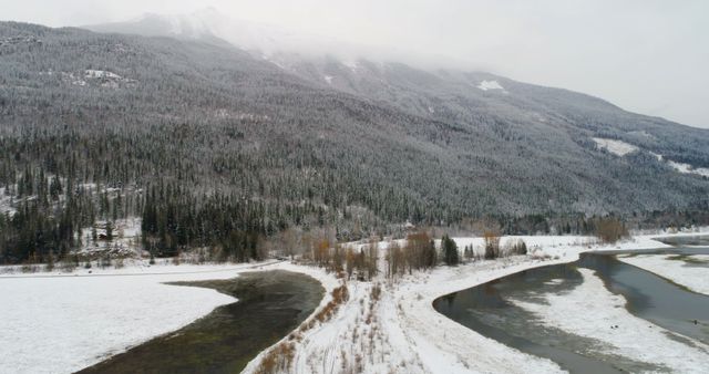 Aerial view of a snowy landscape with a winding river. Outdoor scene captures the serene beauty of a winter forest and river.