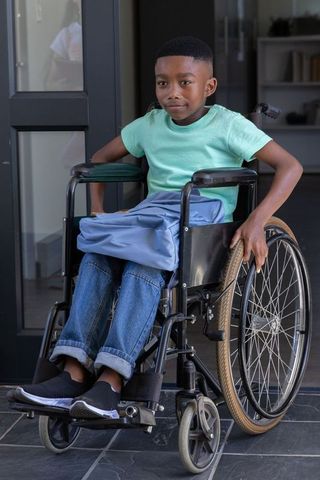 African american schoolboy sitting in manual wheelchair at school entrance gripping wheel