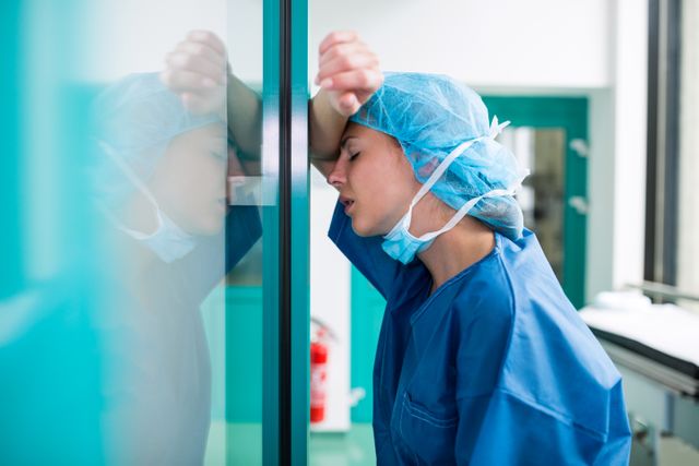 Sad surgeon leaning against the glass door in hospital 