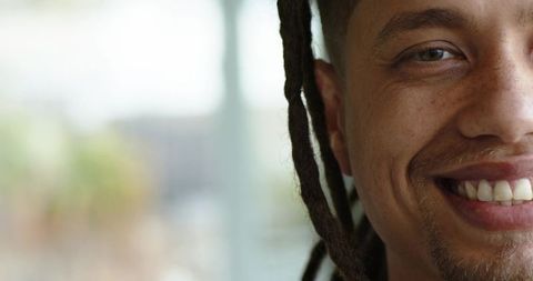 Closeup half-face portrait smiling man with dreadlocks by window natural light and copy space