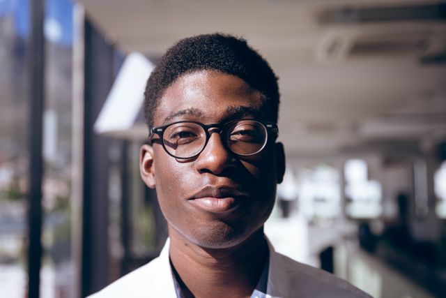 Portrait of happy African American professional businessman working in a modern creative office, wearing glasses and looking at camera. Business office creativity.