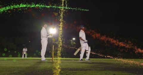 Night cricket batsman walking off pitch under floodlights with wicketkeeper and bokeh lights
