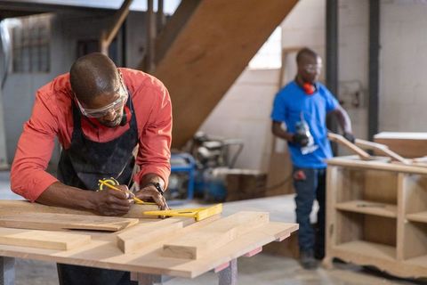 African american carpenter marking wood with square while colleague sands cabinet