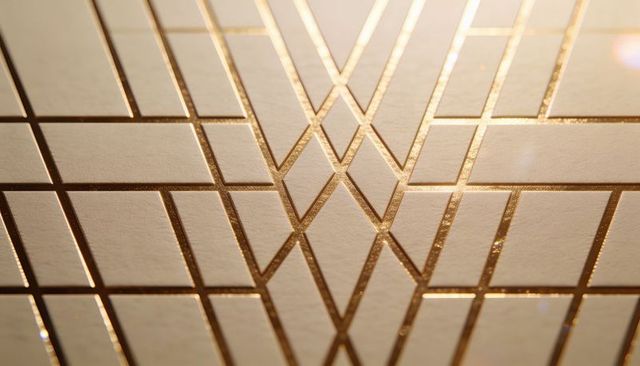 Raised gold foil chevron pattern on textured cardstock catching warm studio light