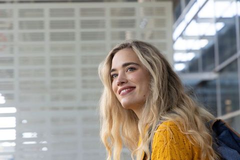 Smiling young woman wearing backpack and mustard knit sweater in modern transit concourse