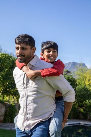 Joyful Indian Father Giving Piggyback Ride to Son by Poolside