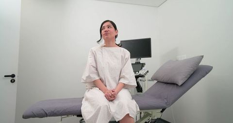 Patient waiting on examination table wearing medical gown in minimalist clinic room