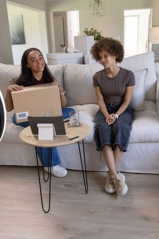 Friends unboxing package on sofa while streaming live reaction in bright modern living room