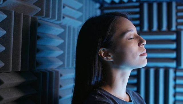 Serene woman meditating in acoustic booth with blue lighting and textured foam panels