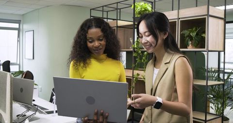 Diverse Coworkers Collaborating on Laptop in Modern Green Office Space