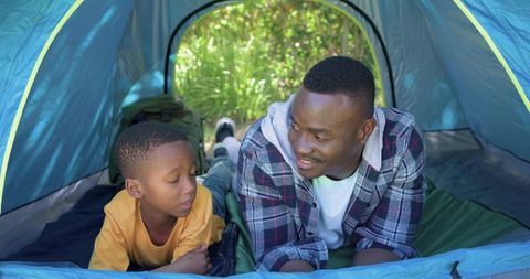 African american father bonding with son camping inside tent on sunny day