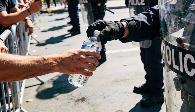 Officer handing water bottle to protester across barricade during urban demonstration
