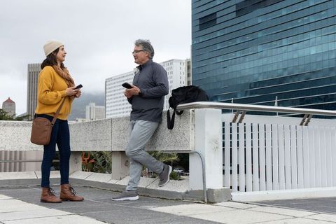 Couple talking on urban overpass holding smartphones, casual fall clothing, city skyline