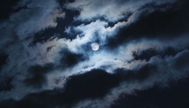 Full Moon Breaking Through Layered Clouds Casting Silver Light Across Moody Night Sky