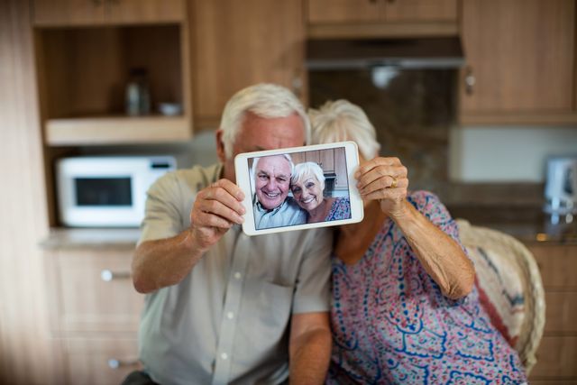 Senior couple taking selfie from digital tablet in kitchen at home