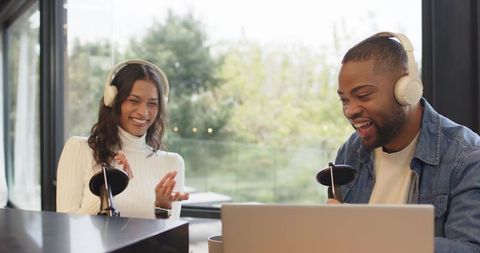 Laughing podcast cohosts recording lively conversation with headphones and microphones