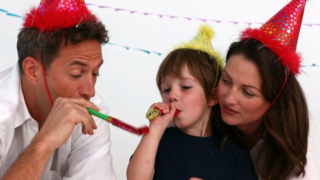 Joyful family celebrating young child's birthday at home, wearing party hats and playing with noise makers. Ideal for advertisements targeting parent-child relationships, family celebrations, parenting blogs, holiday events, and special moments at home.