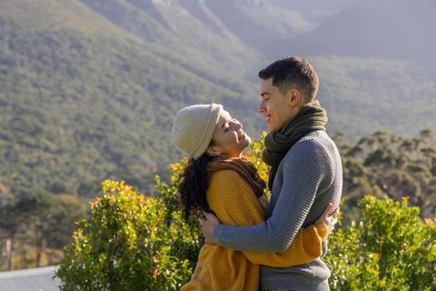 Romantic couple embracing on sunlit hillside wearing cozy sweaters and scarves