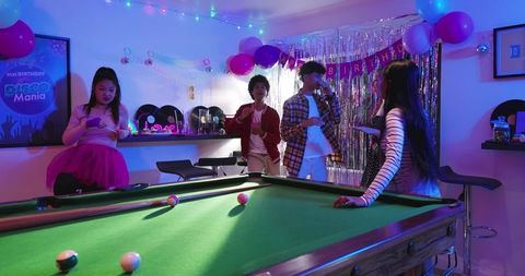Young friends celebrating retro disco birthday in neon-lit game room with pool table