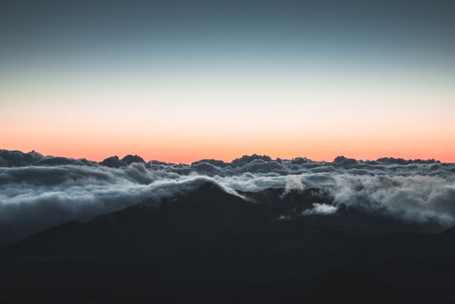 This image captures a peaceful sunrise over mountain peaks partially covered in fluffy clouds. It is perfect for use in travel brochures, inspirational posters, nature blogs, and websites highlighting outdoor beauty. The photo conveys tranquility and could enhance any project related to natural landscapes, meditation, or relaxation.