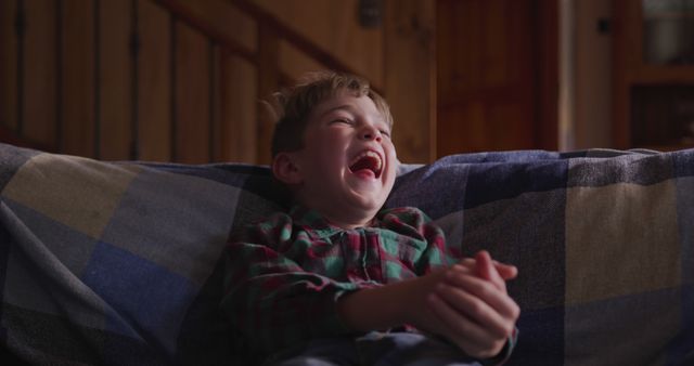 Young boy enjoying time on couch, laughing and showing joy. Good for themes of childhood happiness, family moments, fun at home, carefree childhood days. Ideal for use in advertisements, family-oriented content, children's products, home lifestyle blogs.