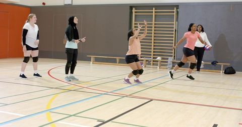 Diverse female athletes practicing indoor volleyball with hijab player, teamwork and coaching