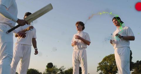 Cricketers chatting and hydrating holding bat during golden hour on grassy field