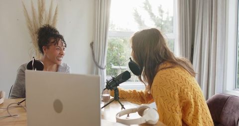 Female cohosts recording casual home podcast with professional microphone and laptop