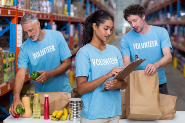 Three volunteers packing eatables in cardboard box in a warehouse